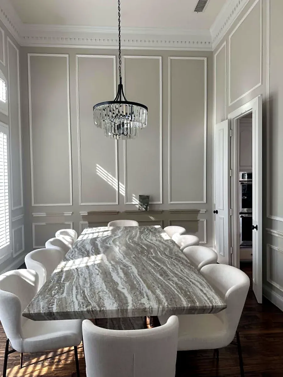 Formal dining room with floor to ceiling wall paneling, a stone top table and a modern chandelier