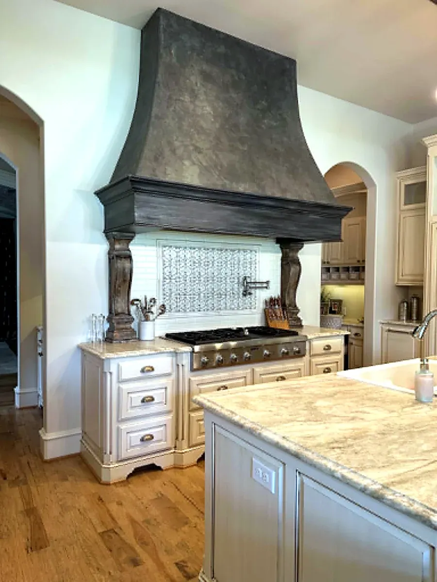 Kitchen with a large custom plaster and wood range hood over a professional range, light cabinetry and hardwood floors