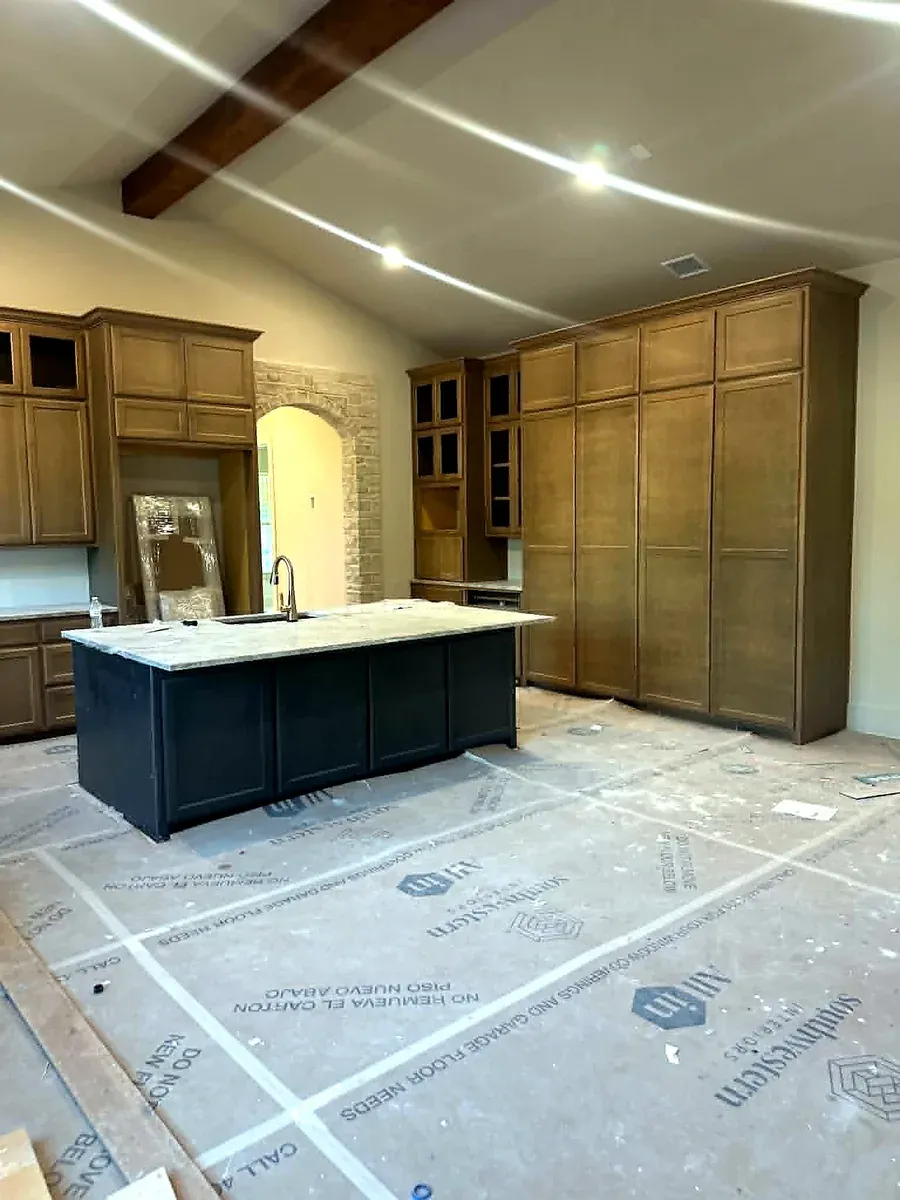 Kitchen remodel underway with cabinetry installed, a stone island in place and protective covering over the finished floors