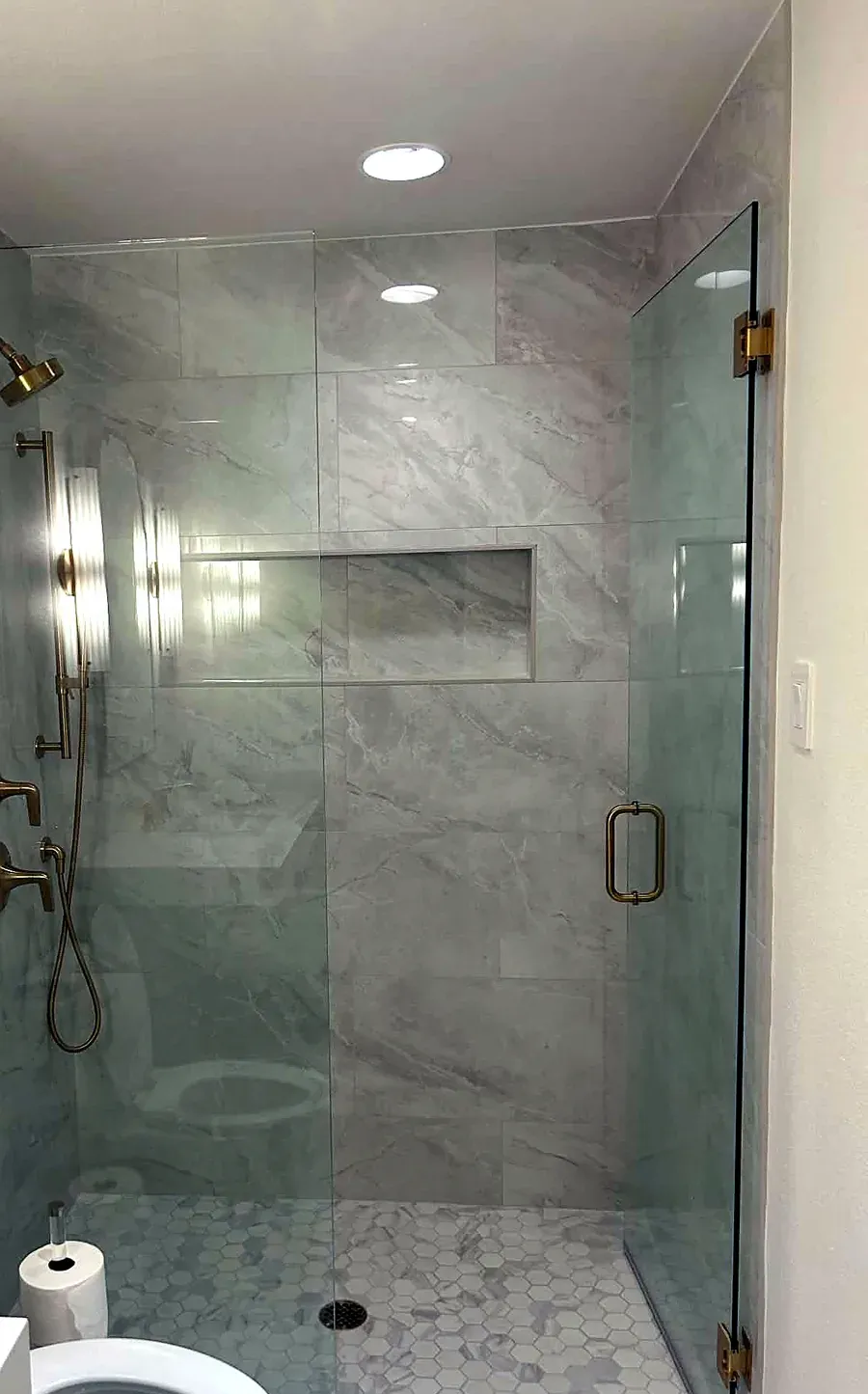 Walk in shower with marble tile walls, a recessed niche, brass shower fixtures and frameless glass