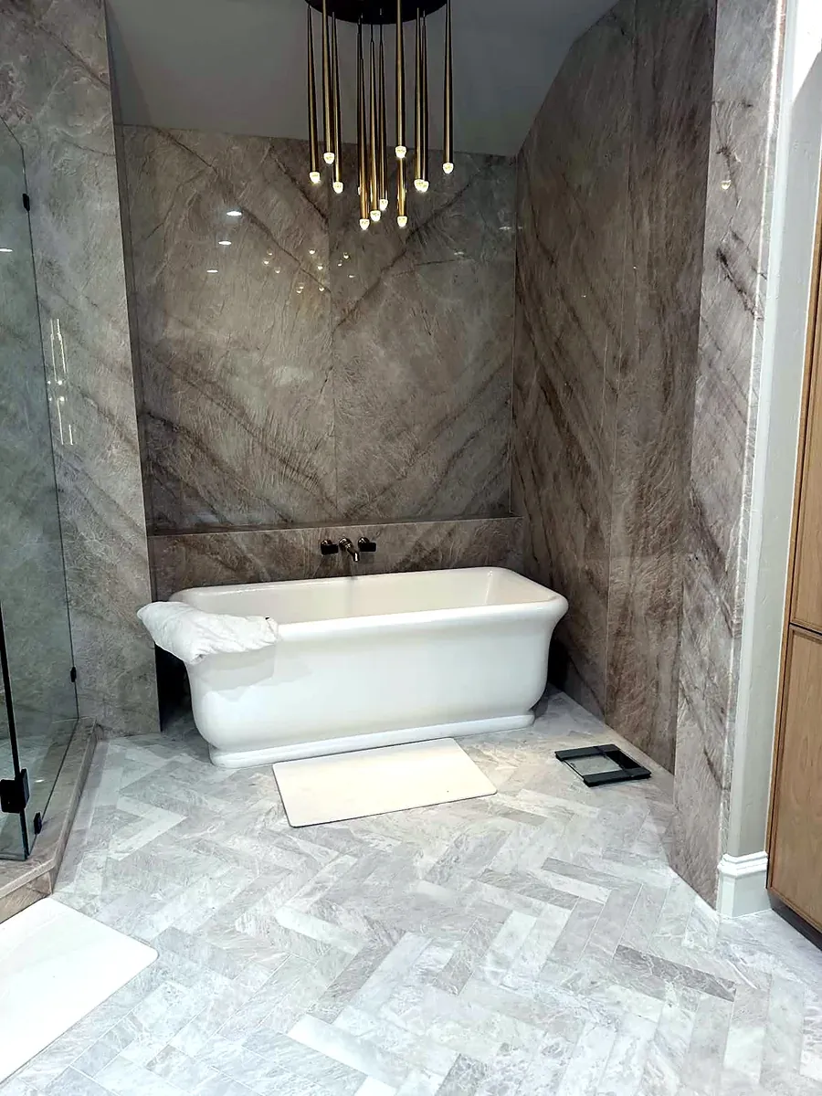 Freestanding soaking tub set into a bookmatched marble alcove with a brass pendant cluster above