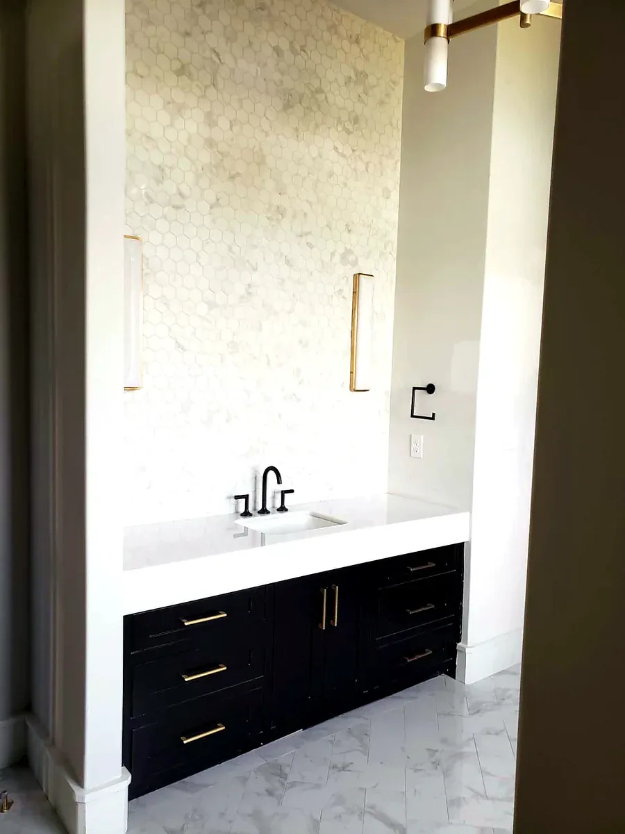Bathroom vanity with black shaker cabinets, brass pulls and a marble slab wall