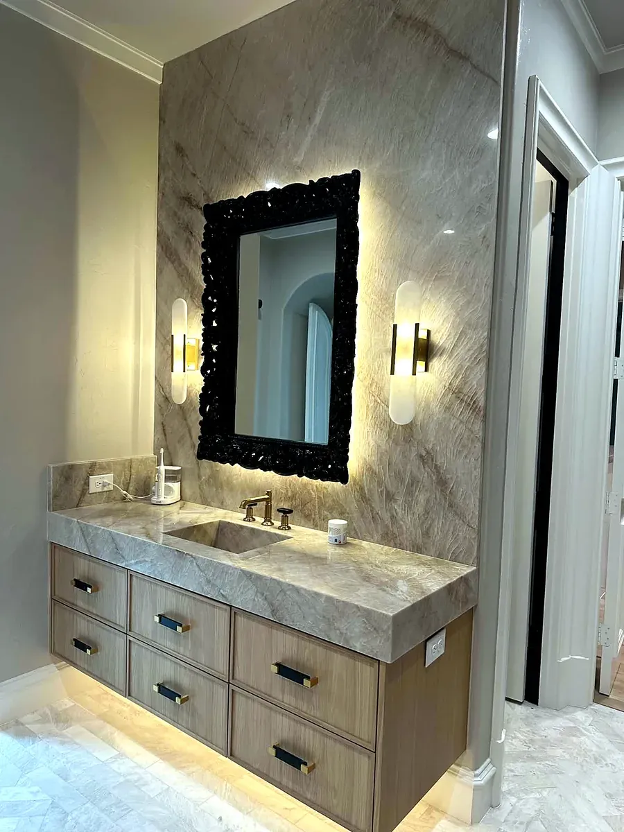Bathroom vanity with a full height marble slab backsplash, black textured mirror and floating oak cabinet
